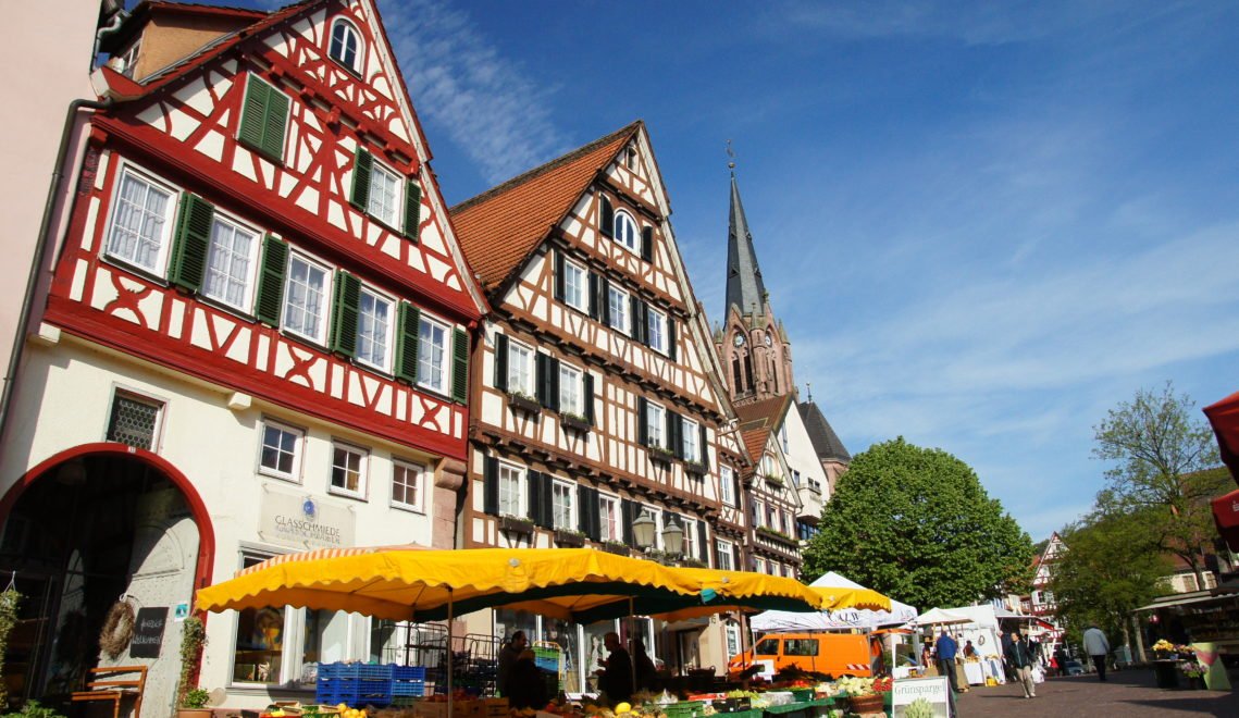 Stalls of a weekly market stand in front of half-timbered houses