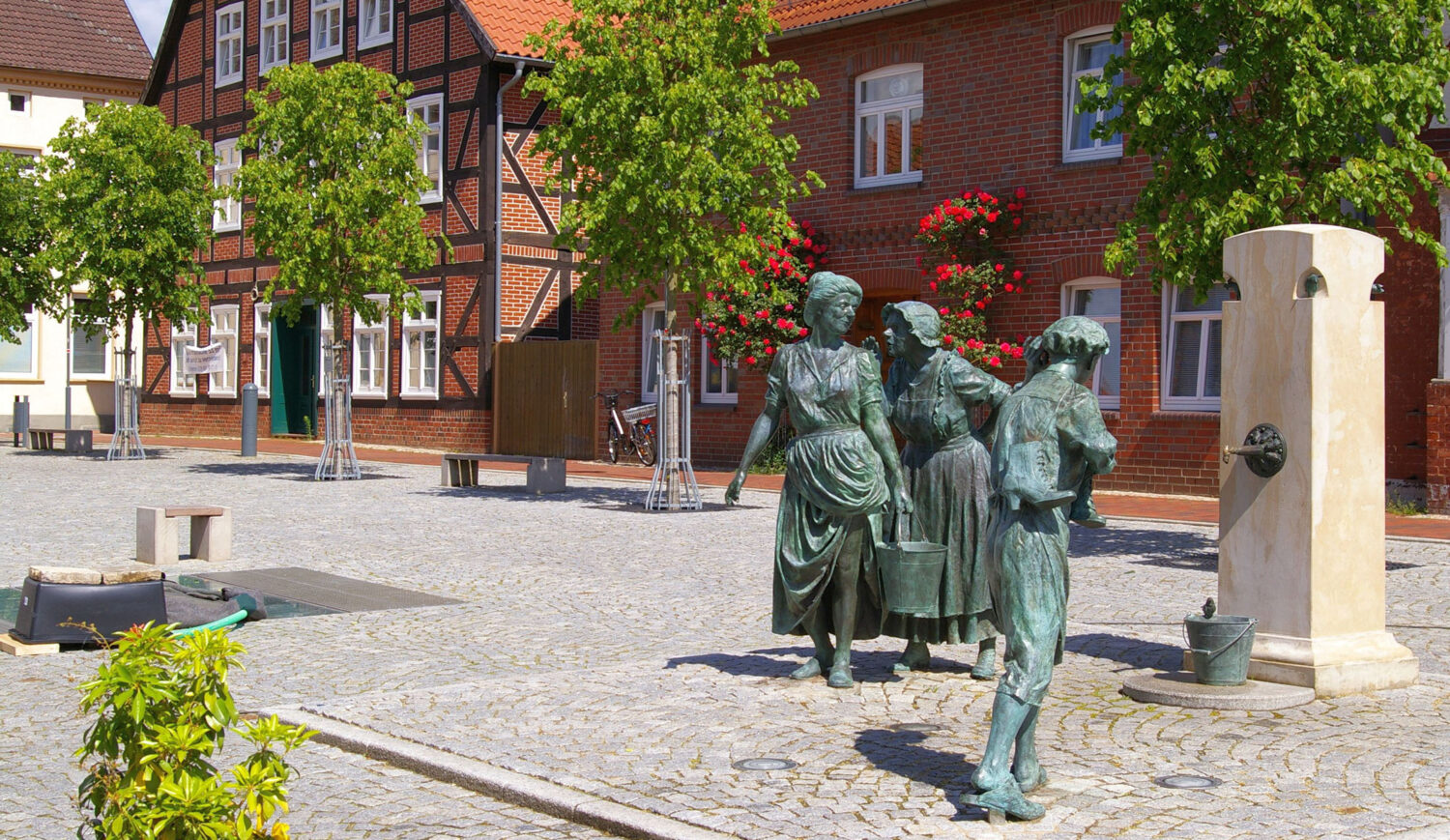 On the town hall market of Hagenow stands the Fiek'n fountain. The scene shows how a merchant whispers the latest gossip from the surroundings into the ear of the maid Sophie